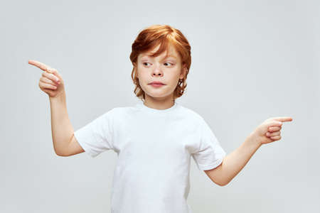 A boy with red hair looks at the index finger and gestures with his hands