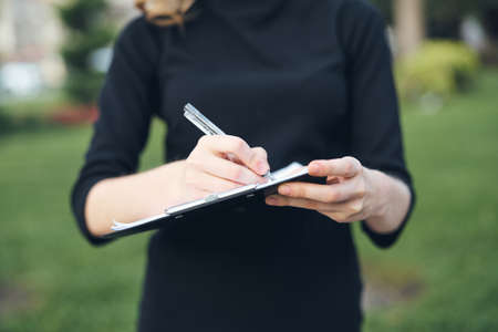 Woman fills out paperwork with pen in hand outdoors cropped viewの写真素材