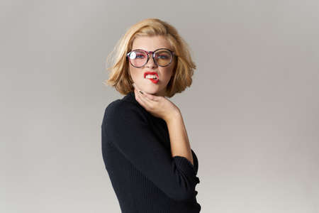 Blonde girl with glasses red lips black blouse cropped view glamor light background studioの写真素材