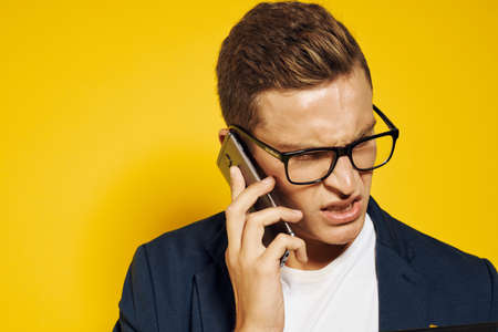 business man at work wearing glasses and a jacket on a yellow background talking on the phone...