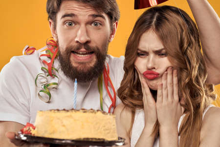 Man and woman birthday festive cake yellow background and caps on the headv