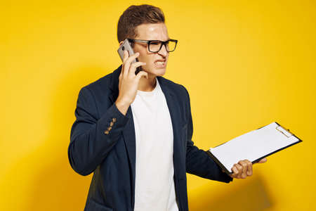 business man at work wearing glasses and a jacket on a yellow background talking on the phone employee modelの写真素材