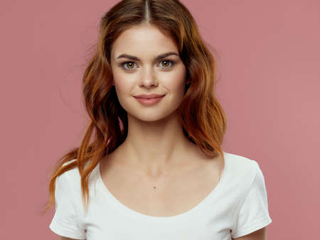 A beautiful girl of European appearance on a pink background looks