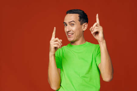 Cheerful man green t-shirts show index fingers up blue isolated background