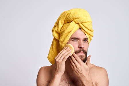 man with a yellow towel on his head bare shoulders sponge clean skin facial care light backgroundの写真素材