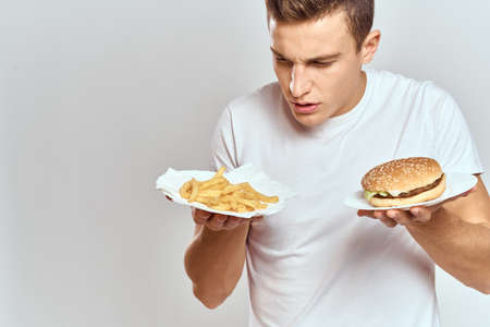 a man with fries and a hamburger on a light background in white t-shirt close-up cropped view Copy Space Modelの写真素材