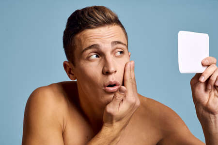 A man examines his face in a mirror on a blue background cropped viewの写真素材