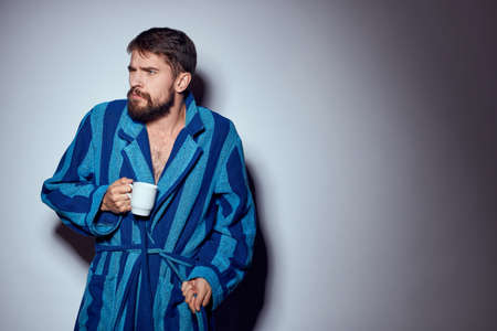 man in a blue robe with a white cup in his hand on a light background gesturing with his hands cropped viewの写真素材