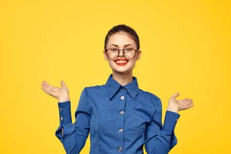 woman with glasses and blue shirt gesturing with her hands on yellow background cropped view Copy...