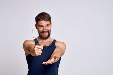 man with a massager for the head and in a blue t-shirt on a light background relaxing beard emotions