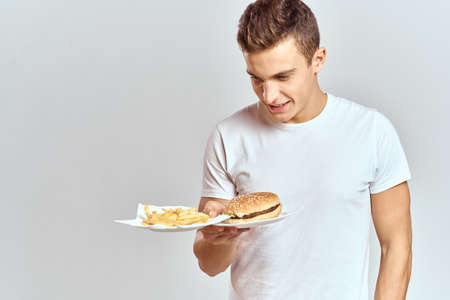 a man with fries and a hamburger on a light background in white t-shirt close-up cropped view Copy Space Modelの写真素材