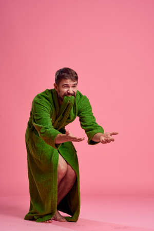 An emotional man in a green robe in full growth on a pink background gestures with his hands to the modelの写真素材