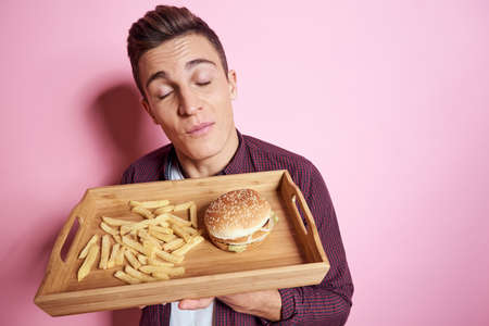 Man with fast food eating hamburger french fries pink background