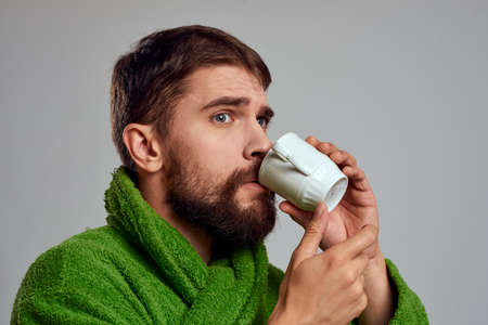 Man in a green robe with a cup of drink in his hands on a gray background cropped viewの写真素材