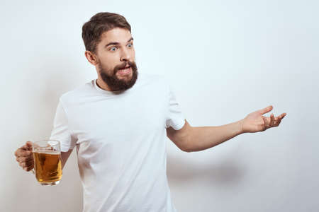man with a mug of beer in his hands and a white t-shirt light background mustache beard emotions modelの写真素材