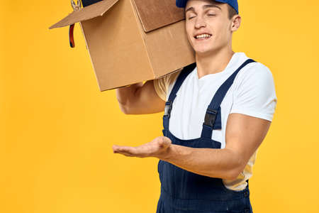 Working man in uniform with box hand delivery loading service yellow background