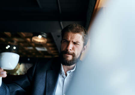 Business man sitting in a cafe with a cup of coffee in his hands in front of a laptop technology...