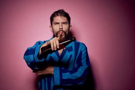 Man in a blue robe with alcohol drinks bottles on a pink background cropped viewの写真素材