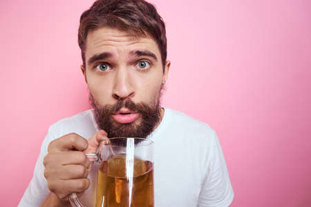 Drunk man with a large mug of beer On a pink background and a white T-shirt relaxed view of a thick beardの写真素材