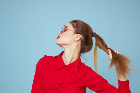 Woman in red shirt on blue background holds hands near face and sunglasses red lips makeup modelの写真素材