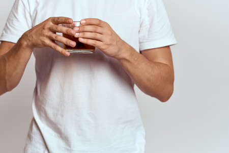 A man with a hot drink of tea in his hands in a white T-shirt on a light background cropped viewの写真素材