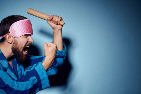 man with rolling pin and in pink sleep mask blue robe cropped view emotion modelの写真素材