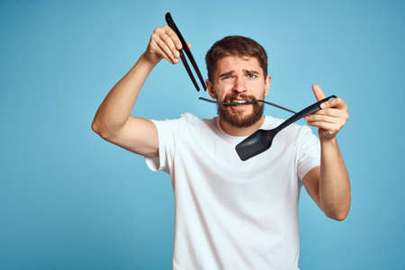 Bearded man with tools for cooking on a blue background and a white T-shirt shovel