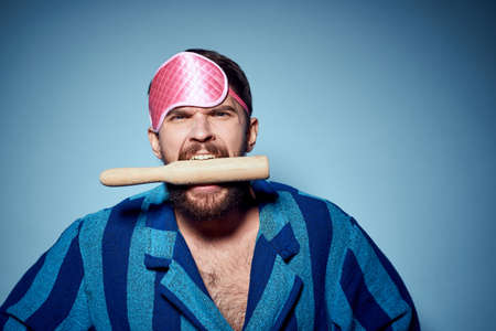 man with rolling pin and in pink sleep mask blue robe cropped view emotion modelの写真素材