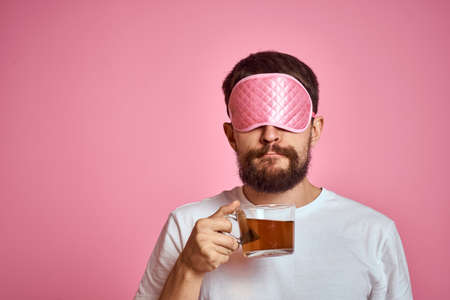 A man in a pink sleep mask with a cup of tea in his hands on an isolated background cropped viewの写真素材