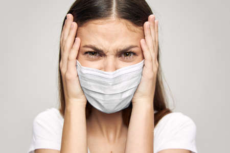 Upset woman in a medical mask touches her face with her handsの写真素材