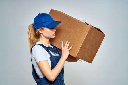 A woman in a working uniform with a box in the hands of a delivery service delivery service light...