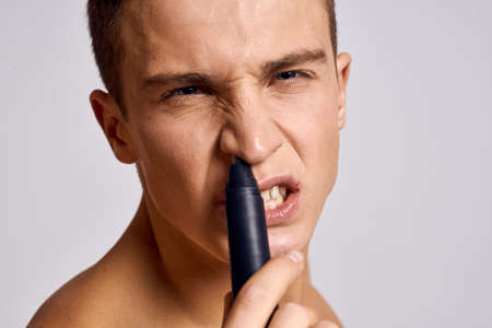 Guy with a trimmer in hand removing hair from the nose naked shoulders emotions light background