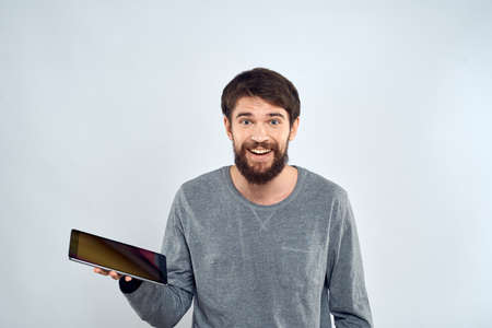 A bearded man with a tablet in his hands a gray jacket technology internet light backgroundの写真素材