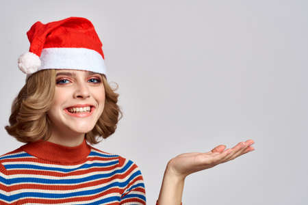 Happy woman in a Christmas cap and a striped sweater gestures with her hands for the New Year holidaysの写真素材