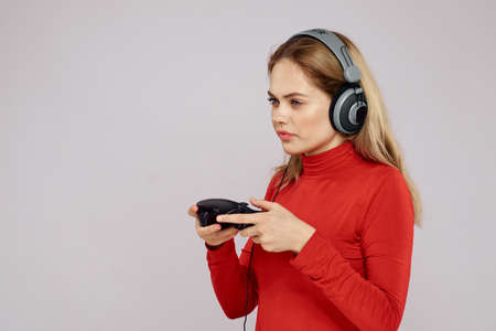 Woman with headphones Joystick in hands playing games fun leisure lifestyle entertainment red shirt gray backgroundの写真素材