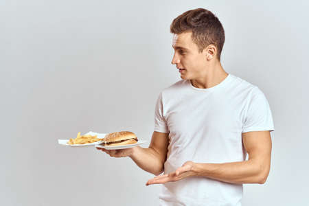 a man with fries and a hamburger on a light background in white t-shirt close-up cropped view Copy Space Modelの写真素材