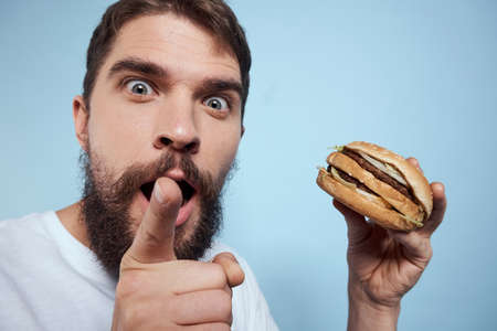 Emotional man hamburger fast food diet food close-up blue background