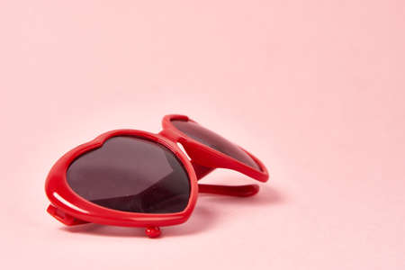Heart shaped sunglasses with red frames on a pink background