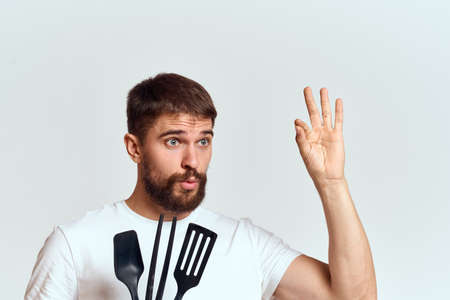 A man with kitchen appliances in the hands of their white T-shirt on a light background cropped view
