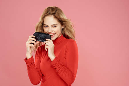 Woman with gamepad in hand entertainment video games lifestyle technology red blouse pink backgroundの写真素材