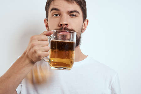 A bearded man with a mug of beer on a light background in a white T-shirt cropped view of an alcoholic drinkの写真素材