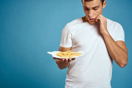 man with fries in cardboard plate calories fast food blue background teen model cropped viewの写真素材