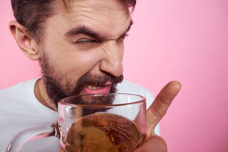 Drunk man with a large mug of beer On a pink background and a white T-shirt relaxed view of a thick beardの写真素材