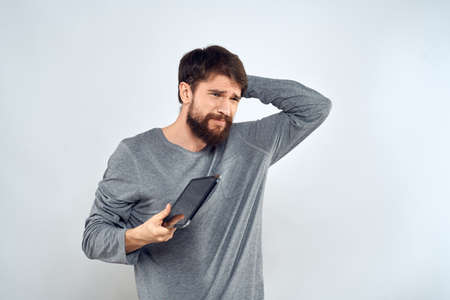 A bearded man with a tablet in his hands a gray jacket technology internet light background