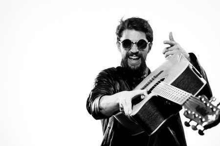 A man plays the guitar in a black leather jacket with sunglasses on a light backgroundの写真素材