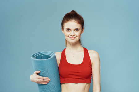 Sportive woman training mat in hands Red tank top exercise blue backgroundの写真素材
