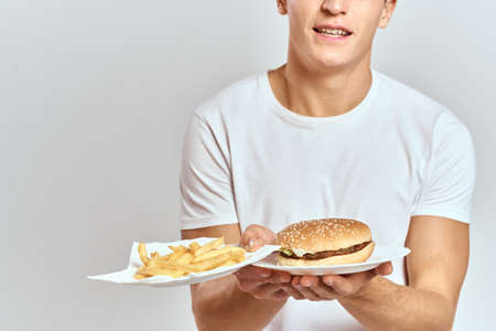 a man with fries and a hamburger on a light background in white t-shirt close-up cropped view Copy Space Modelの写真素材