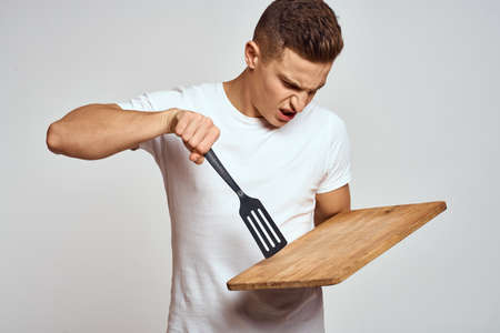Guy with kitchen tools in hands on a light background cropped view of emotions fun modelの写真素材