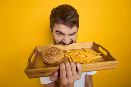 Man with wooden pallet fast food hamburger french fries diet food intake close-up