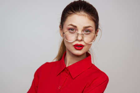 fashionable woman in a red shirt on a light background fun emotions bright makeup glasses attractive appearanceの写真素材